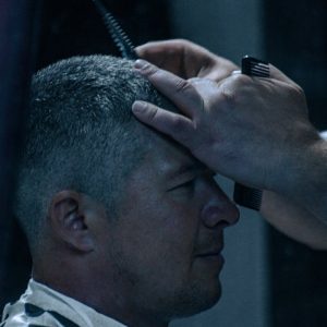 Close-up of a barber styling hair of a male client using scissors and comb in a dim-lit barbershop.